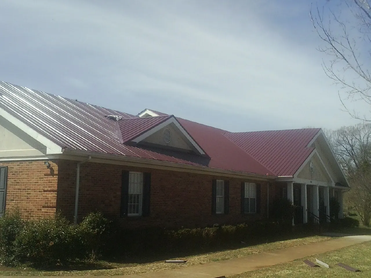 Red metal roof with gabled entries on a long brick building, from a Hail Damage Roof Repair job in Hiko