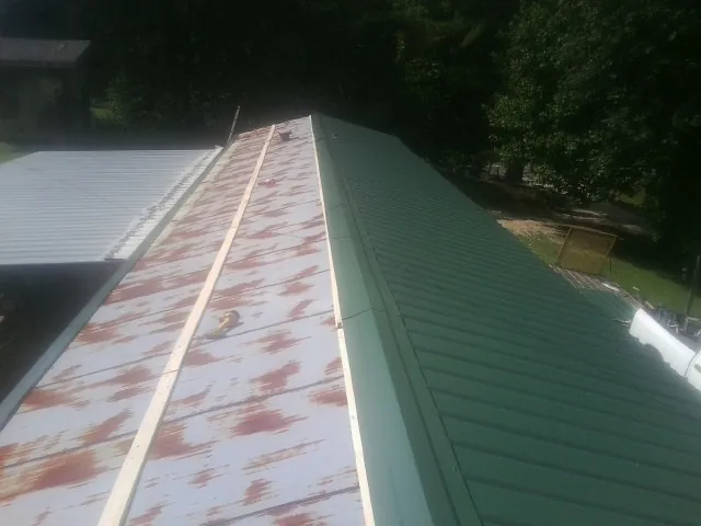Old rusted panels beside newly installed green metal roofing — Wind Damage Roof Repair by Roofing Brothers in Hiko