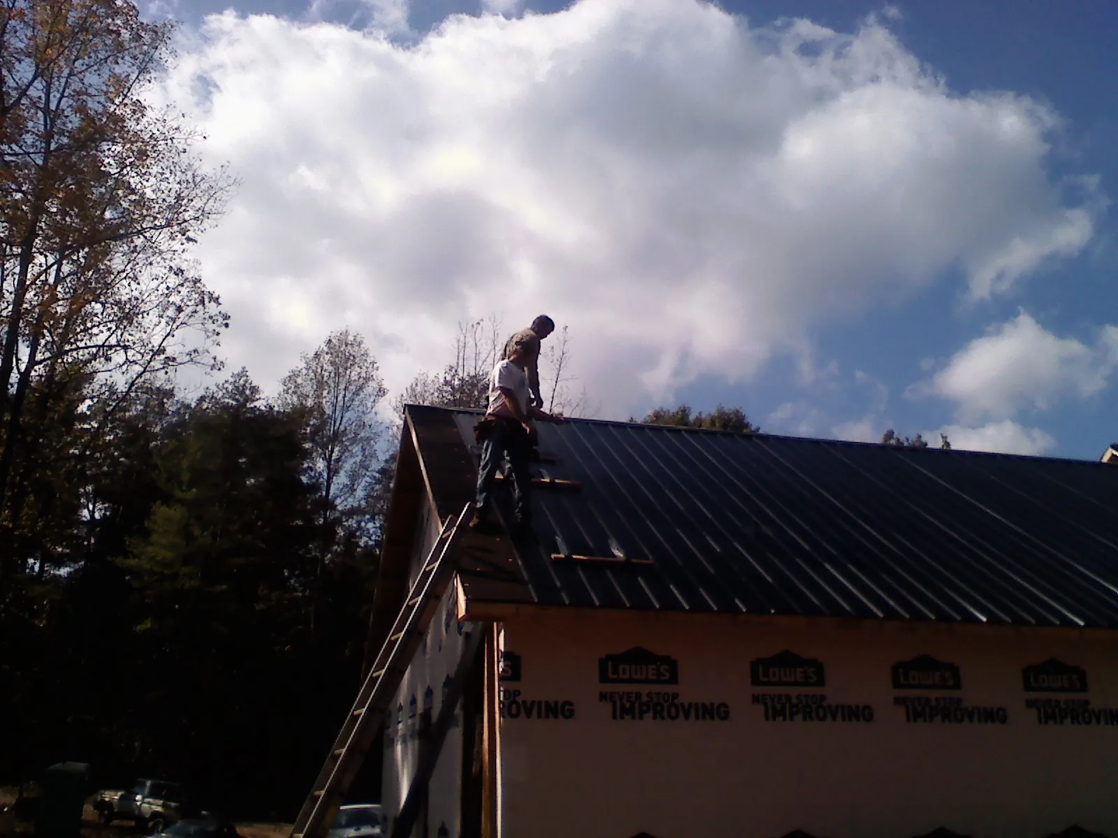 Roofer fastening dark metal panels high against a cloudy sky, from a Roof Inspection job in Hiko